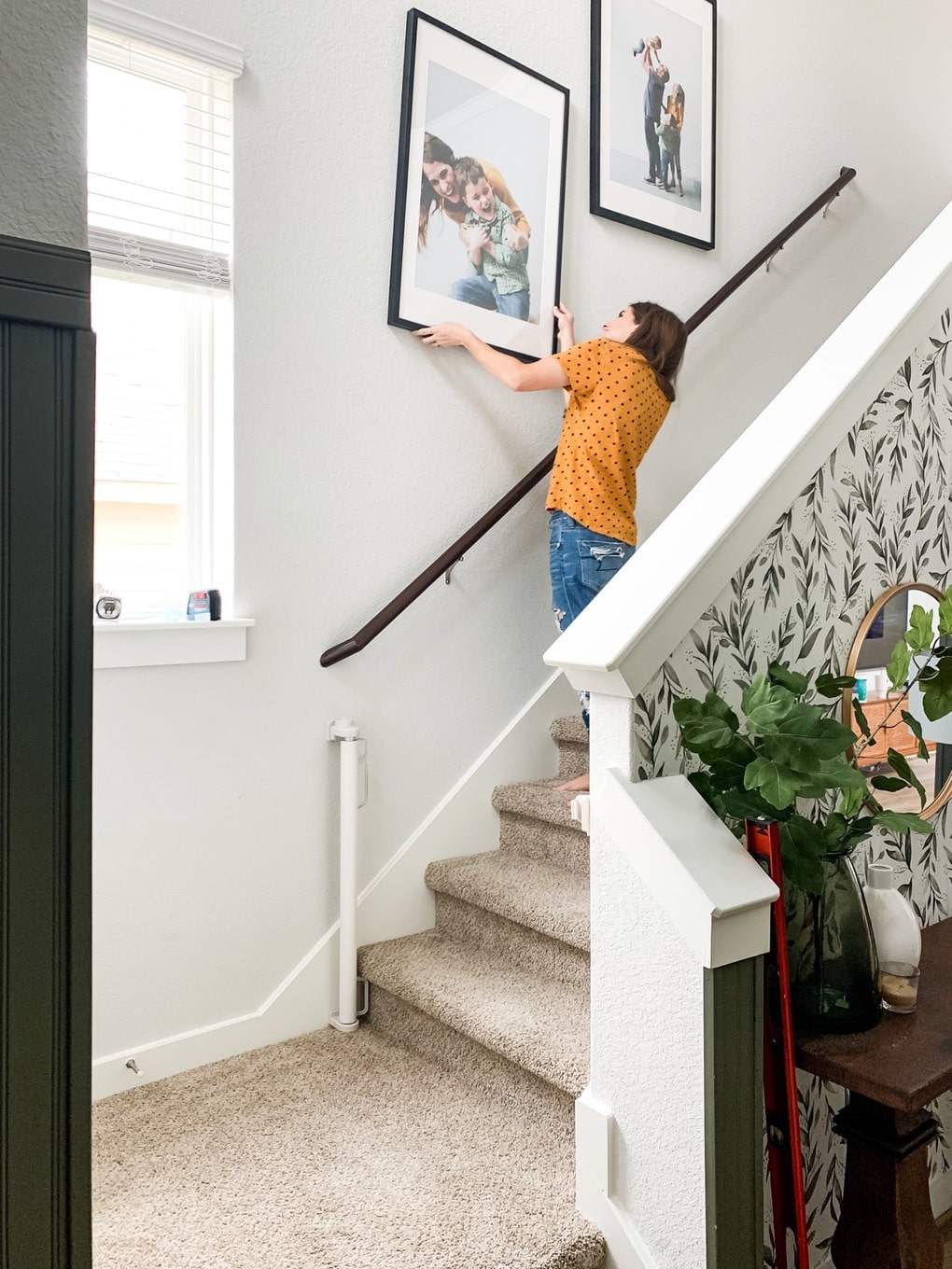 Woman hanging a large frame on her stair wall