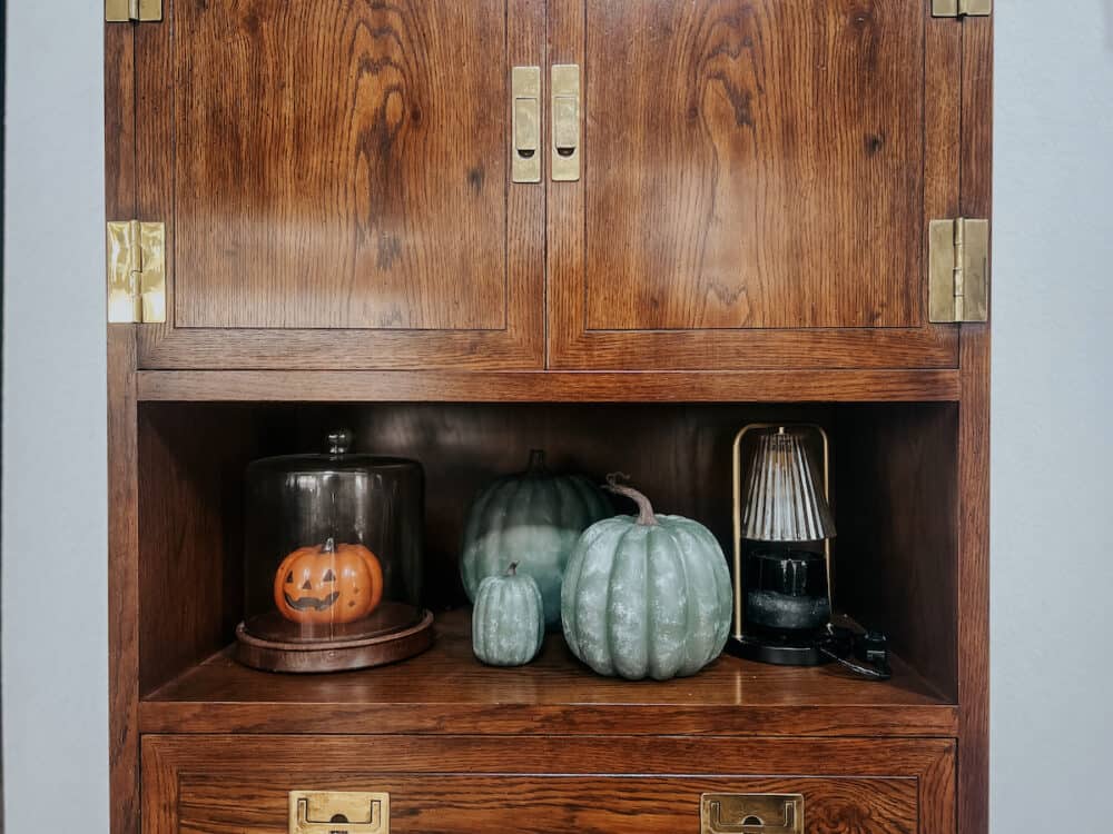 A bar cabinet with faux stone look painted pumpkins on a shelf