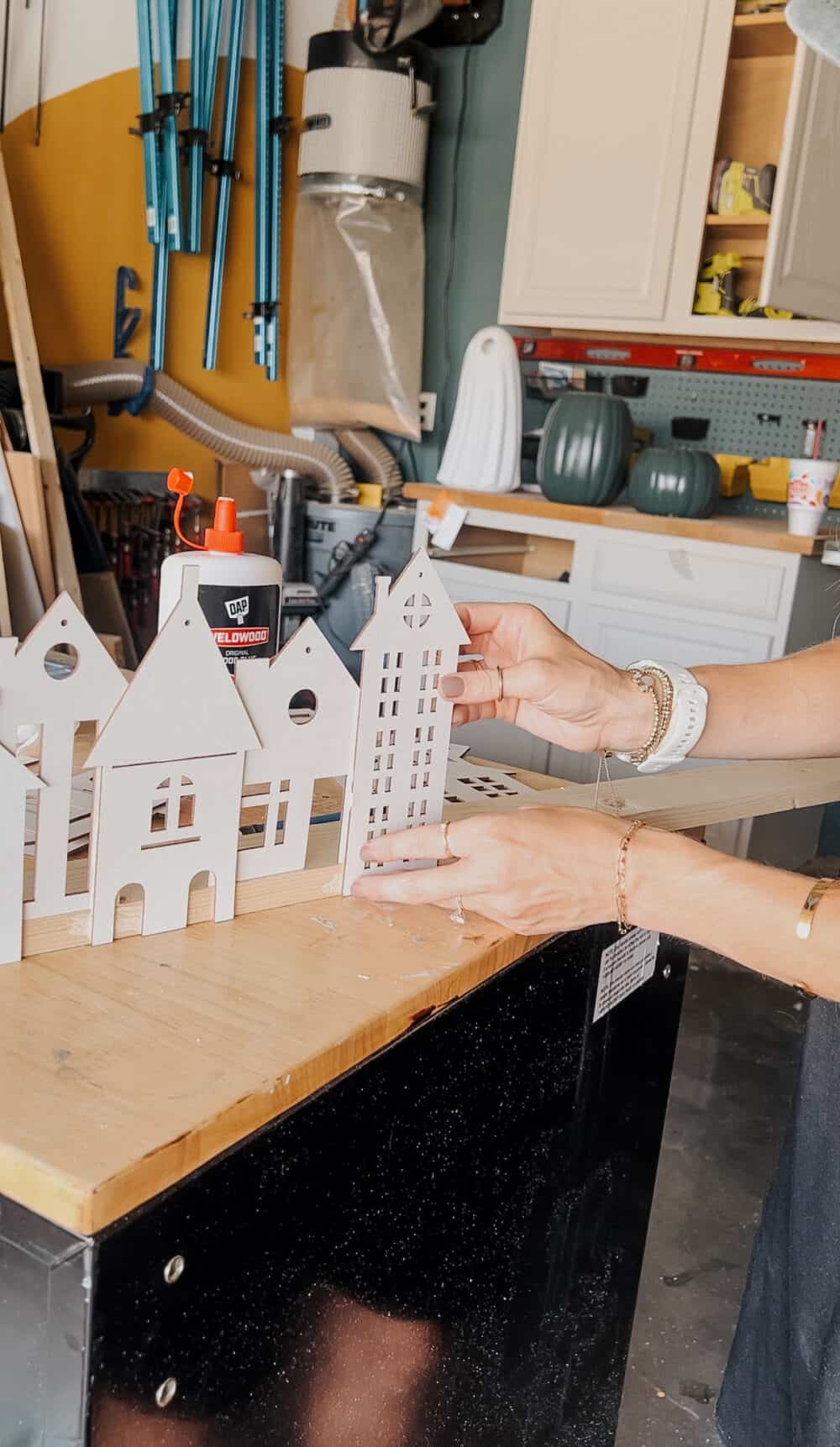 woman's hands gluing a wood house to a piece of scrap wood 