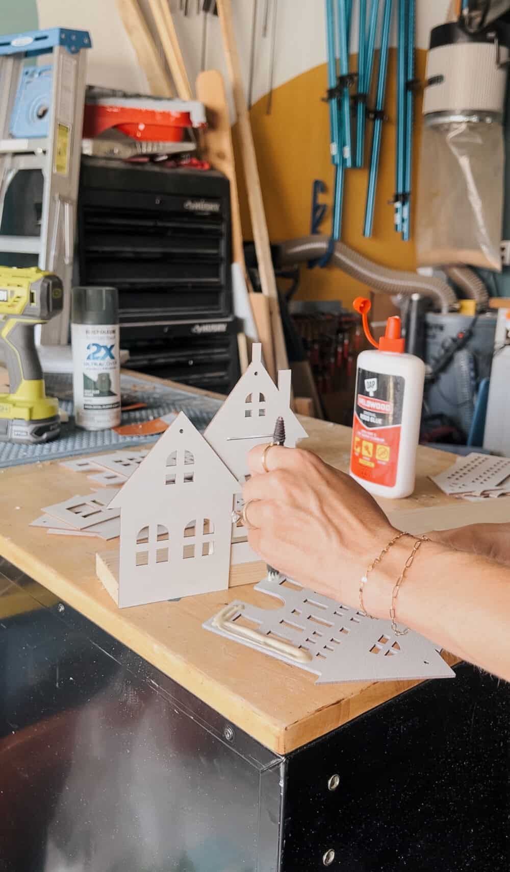 woman's hand applying wood glue to a small wood house